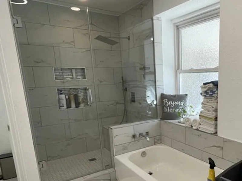 The Same Bathroom, Finished — Marble-look tile carried through the shower, the niches, the tub surround and the window ledge.
