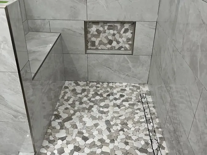 Walk-In Shower — Large-format wall tile with a split-stone pebble floor, built-in bench, recessed niche and a linear drain.