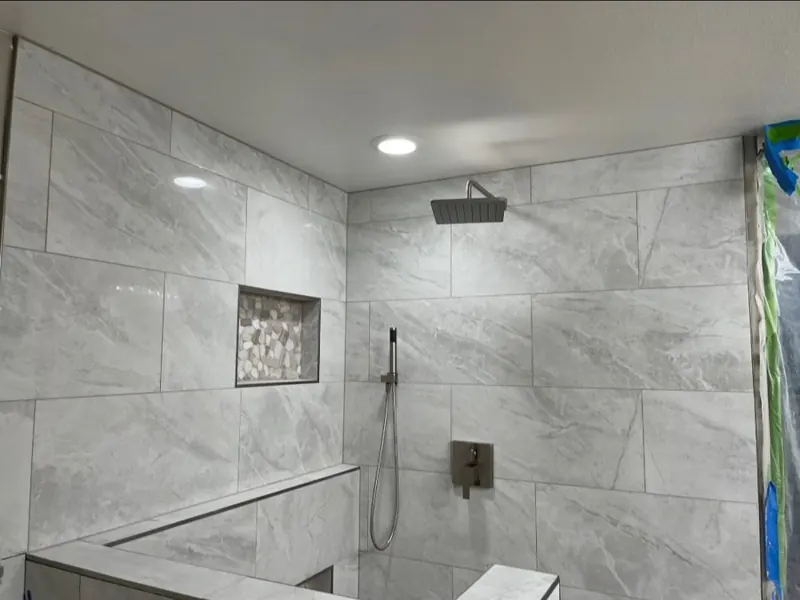 Same Shower, Looking Up — Rain head and handheld valve set into the wall tile, with the niche trimmed in matching pebble.